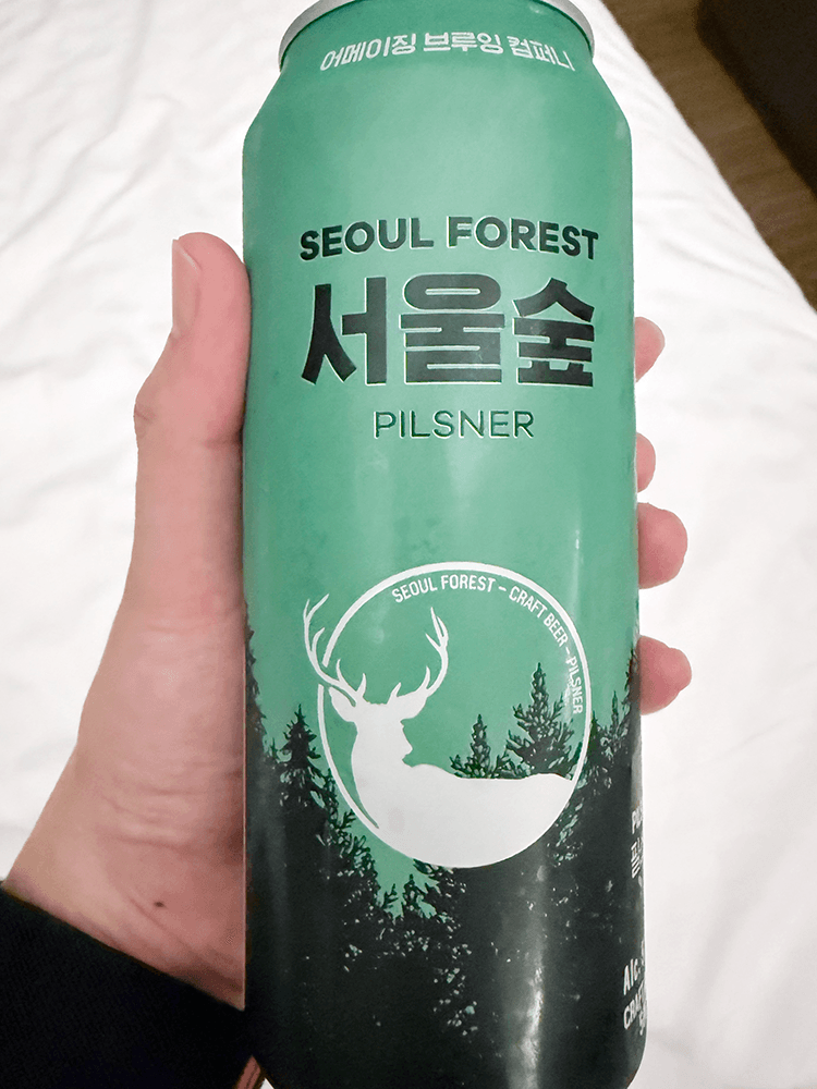a can of beer that written as Seoul Forest pilsner. Light green, black woods silhouette are bottom of the can. There are white deer silhouette logo on the middle of the can.