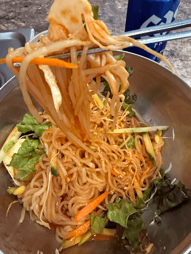 mixed and turned red noodles by sauce are pulled up by silver stainless chopsticks