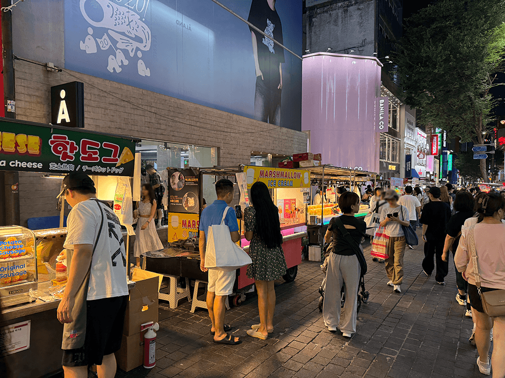 close up to the food stands. There are hot dog, marshmallow ice cream stands and some others. People are stopping by stands others are walking.